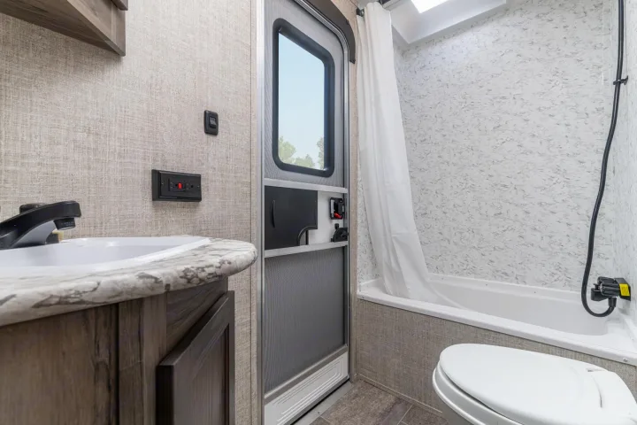 Inside a functional RV rental bathroom featuring a sink, toilet, shower/tub, and secure entry door.. Gulf Stream Ameri-Lite 2024