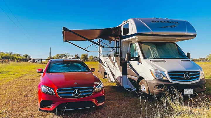 Sunny day RV rental setup: a red Mercedes car and a white Sunseeker RV parked in a green field.. Forest River Sunseeker MBS 2019