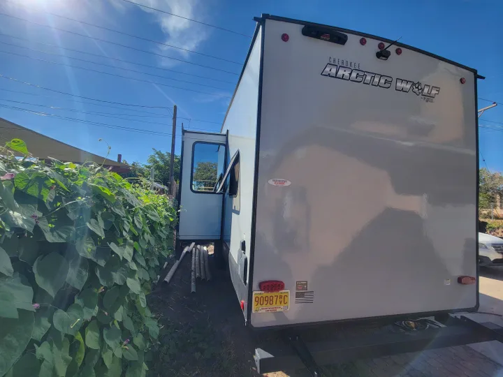 Rear and side view of a white Cherokee Arctic Wolf travel trailer, ideal for an rv rental, parked next to green foliage.. Forest River Cherokee Arctic Wolf 2023