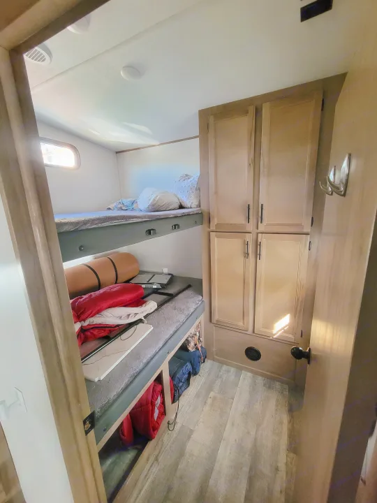 RV rental interior: cozy bunk beds with bedding, storage cabinets, and wood-look flooring for comfortable travel.. Forest River Cherokee Arctic Wolf 2023