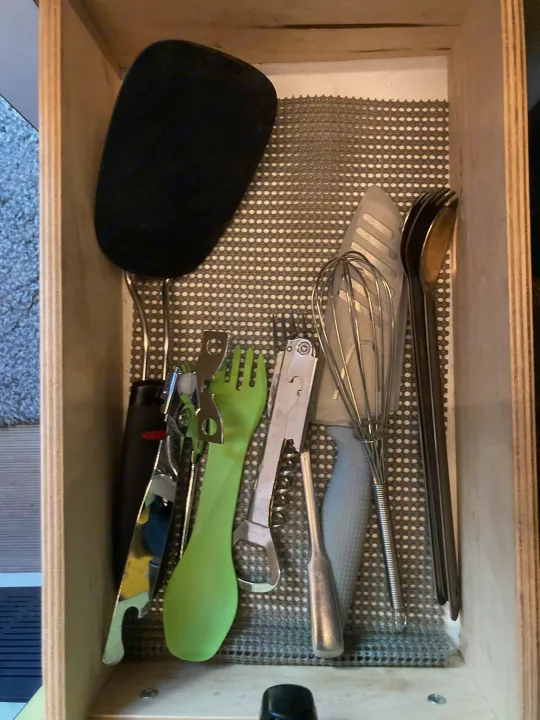 Essential kitchen tools for your RV rental: spatula, whisk, can opener, corkscrew, and cutlery neatly arranged in a lined drawer.. Winnebago Revel 2020
