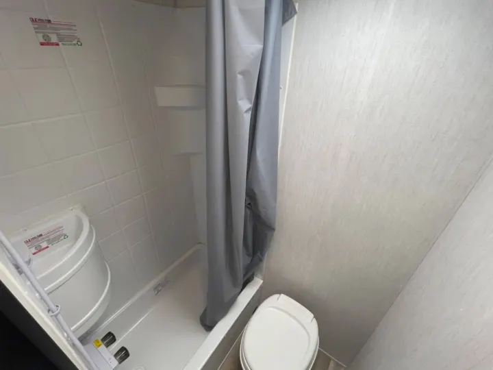 Inside an RV rental: a compact bathroom featuring a shower with curtain, toilet, and corner sink.. Forest River Cherokee Wolf Pup Black Label 2022