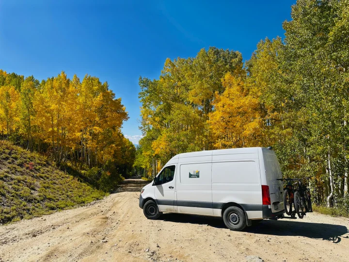 Autumn adventure: A white **rv rental** van with bikes on a dirt road surrounded by golden aspens.. Mercedes-Benz Sprinter 2021