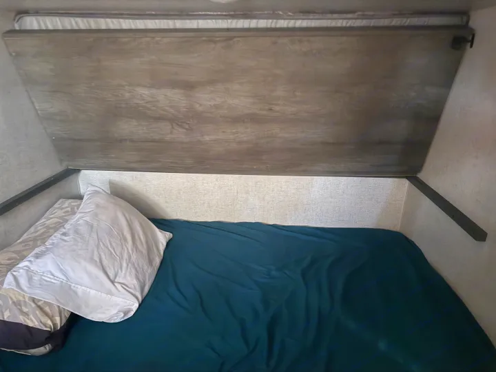 RV rental bunk bed with a dark teal sheet and pillows, tucked under a wooden panel. A compact and functional sleeping area.. Forest River Other 2021