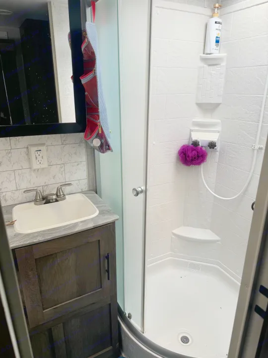 Inside an RV rental bathroom: compact sink, dark cabinet, and a clean shower with shampoo and a loofah.. Forest River Other 2021