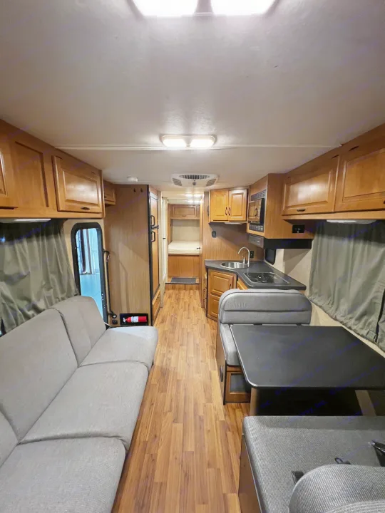 Inside an RV rental, showing the living area with a sofa, dining table, kitchen, and rear bunk beds.. Thor Majestic 2019