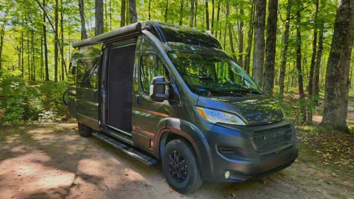 Dark green Airstream camper van, ideal for an RV rental, parked on a dirt path in a sun-dappled forest.. Airstream Rangeline 2024