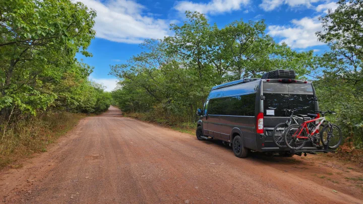 Adventure awaits! Dark grey RV rental parked on a dirt road in a sunny forest with bicycles on the back, ready for exploration.. Airstream Rangeline 2024