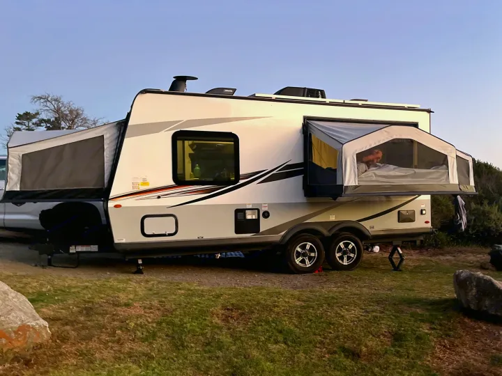 This RV rental shows a hybrid travel trailer expanded for camping with its pop-out tent beds, one occupied by a sleeper.. Rockwood Roo 2022