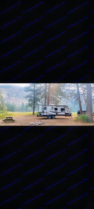 Scenic campsite with an RV rental travel trailer, picnic table, fire pit, surrounded by pine trees and hazy mountains.. Keystone RV Cougar 2015