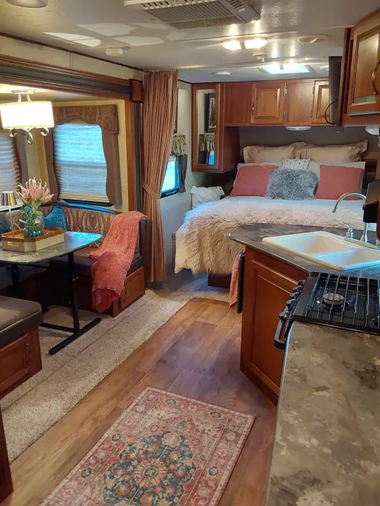 RV rental interior: Cozy bedroom with fluffy bedding, kitchen with sink/stove, and dining nook visible.. Keystone RV Cougar 2015