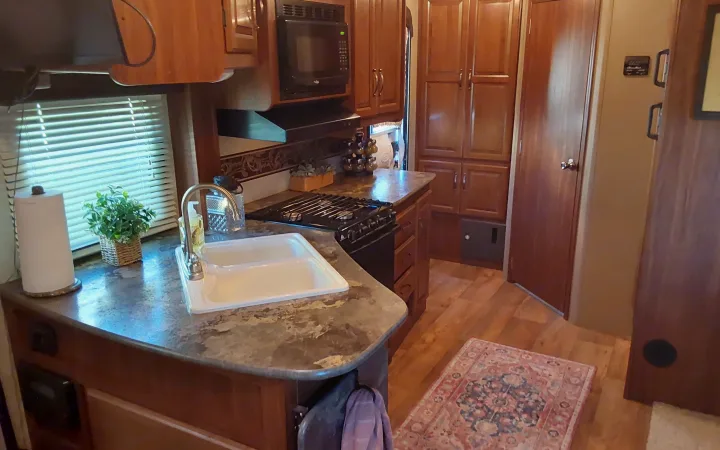 Inside your RV rental: a functional kitchen with a sink, stovetop, microwave, and warm wooden cabinets for comfortable travel.. Keystone RV Cougar 2015