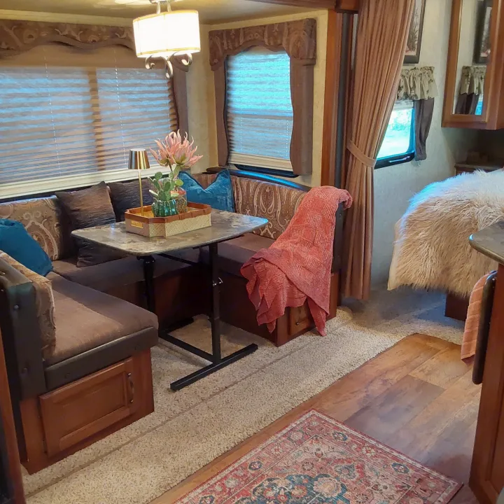 Inside a comfortable RV rental: dinette with patterned cushions, decorative lamp, & cozy bedroom with fluffy blanket and laminate floor.. Keystone RV Cougar 2015