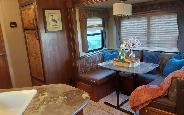 RV rental interior featuring a cozy dinette with blue pillows, kitchen sink, wood-paneled fridge, and art decor.. Keystone RV Cougar 2015