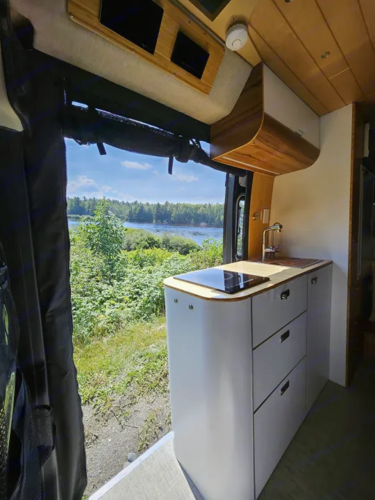 RV rental: Modern camper van kitchen with sink, induction cooktop, and a scenic river view outside.. Noovo Pop 2024