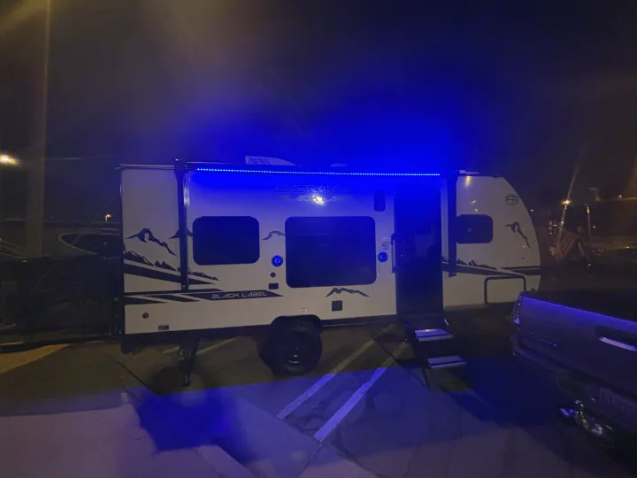 Nighttime rv rental: A white Cherokee Black Label travel trailer with vibrant blue LED awning lights, parked beside a truck.. Forest River Wolf Pup 2025
