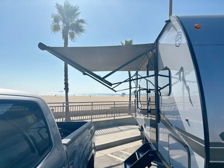 Beach day with an RV rental! Awning extended for shade, overlooking the sunny ocean, sand, and palm trees.. Forest River Wolf Pup 2025