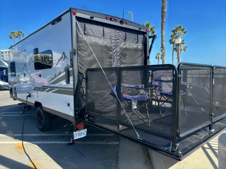Sunny rv rental toy hauler with its rear ramp converted into a patio deck, featuring chairs and a mesh screen, near palm trees.. Forest River Wolf Pup 2025
