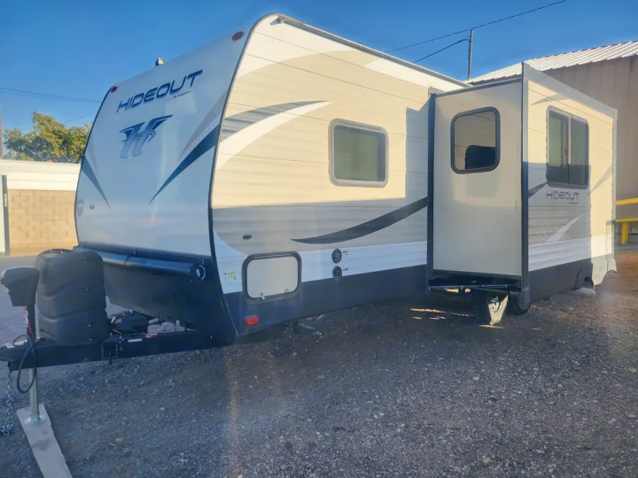 Light-colored Hideout travel trailer with extended slide-out for rv rental, parked on gravel.. Keystone RV Hideout LHS 2019