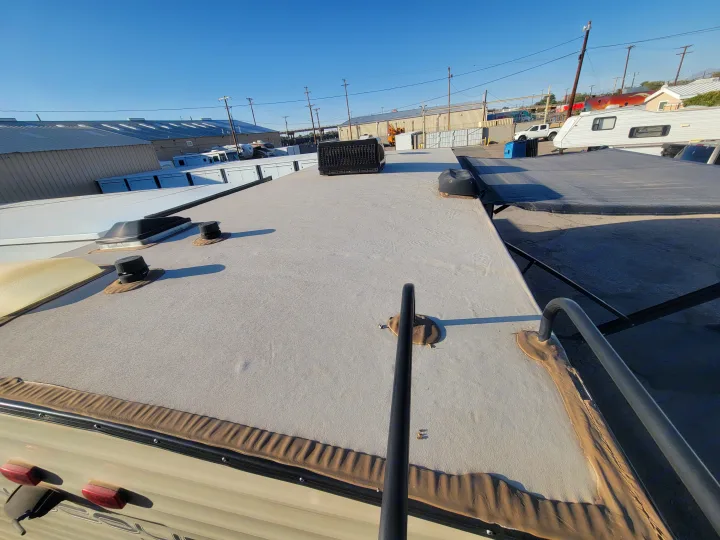 Looking forward from an RV rental's rooftop, featuring the grey textured surface, various vents, and a distant AC unit.. Keystone RV Hideout LHS 2019