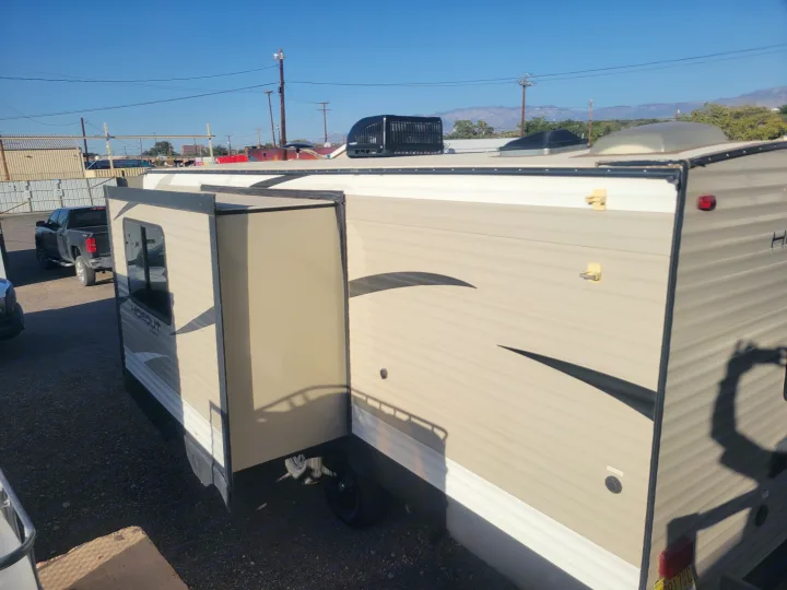 Tan RV rental with extended slide-out parked outdoors, ready for travel. Sunny sky and mountains visible.. Keystone RV Hideout LHS 2019