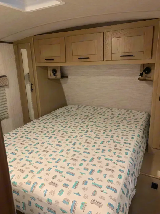 RV rental bedroom with camper-themed sheets, overhead storage, and reading lights, ideal for travel.. Heartland RVs Sundance Ultra Lite 2021