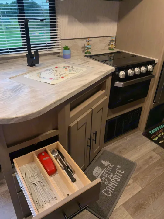 RV rental kitchen: modern black faucet, stove, open drawer with cutlery. Ready for camping trips!. Heartland RVs Sundance Ultra Lite 2021