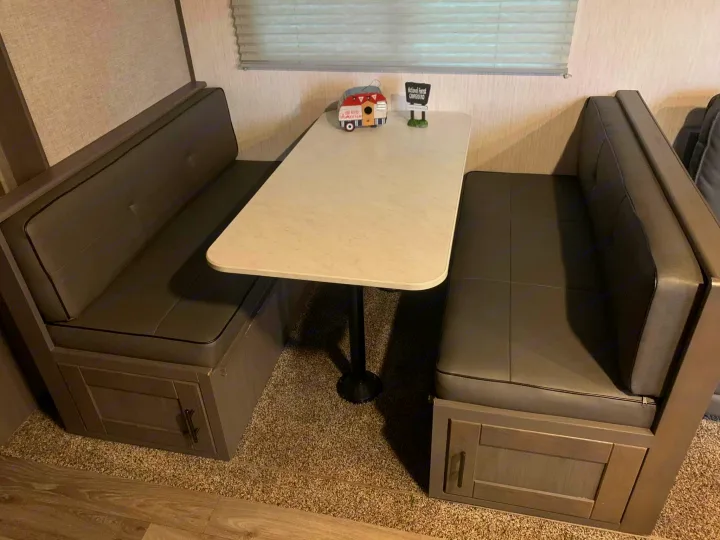 Cozy RV rental dinette featuring grey booth seating, a center table, and charming camper decor by the window.. Heartland RVs Sundance Ultra Lite 2021