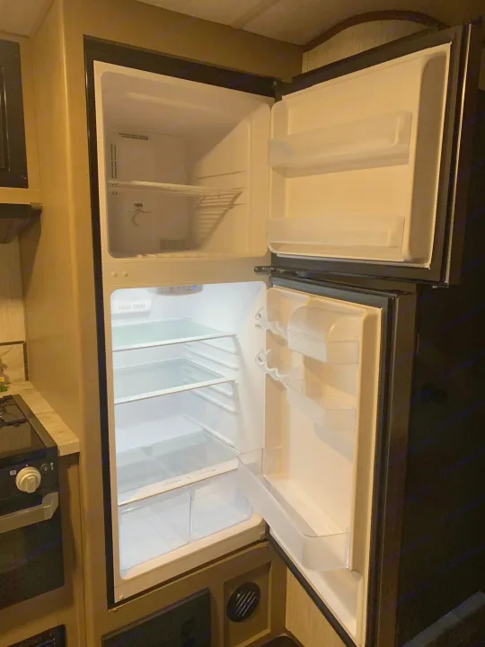 Inside an **rv rental**, a clean, empty two-door refrigerator with clear shelves is ready for your travel essentials.. Heartland RVs Sundance Ultra Lite 2021