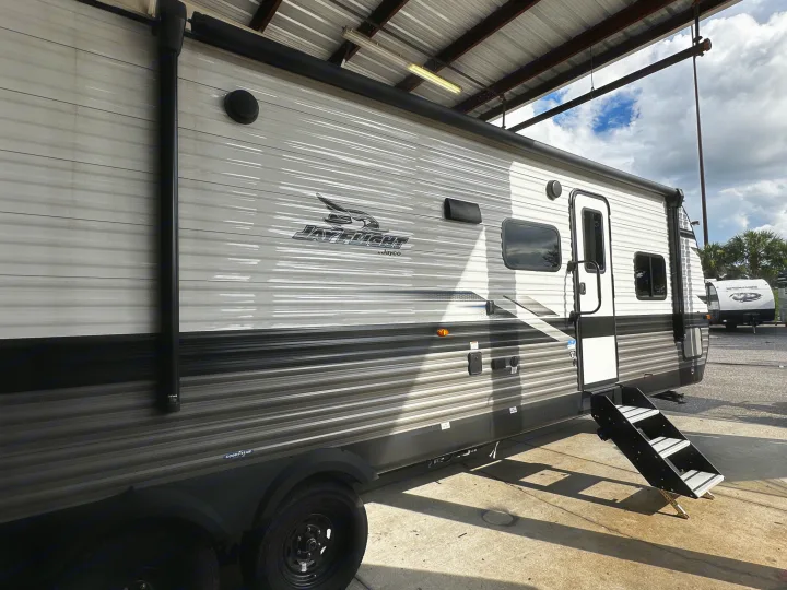 A white and grey Jayco travel trailer, an ideal RV rental, parked under a shelter on concrete with steps extended.. Jayco Jay Flight 2024