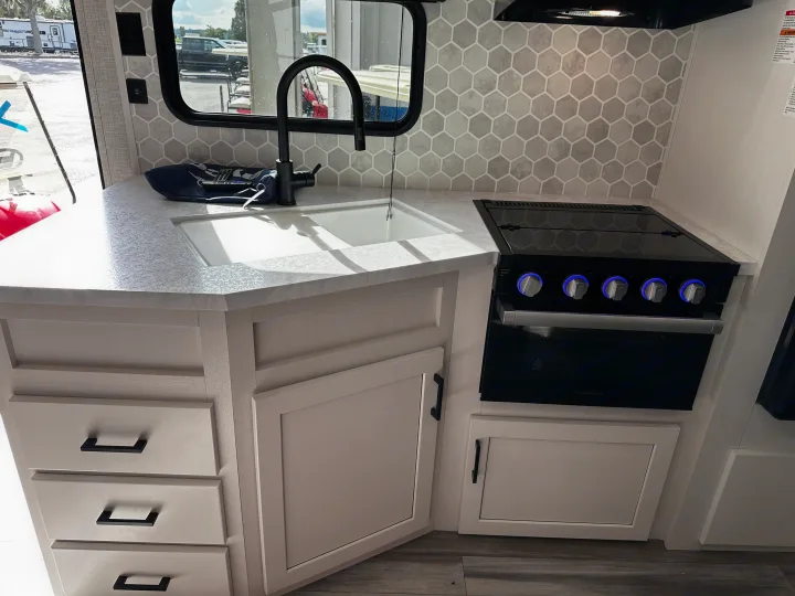 Inside an RV rental: a modern kitchen featuring a black faucet, Furrion stove, and light cabinets with hexagonal backsplash.. Jayco Jay Flight 2024