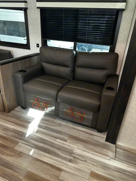 Comfortable RV rental living space featuring a dark sofa with cupholders, pleated blinds, and wood-grain floor.. Jayco Jay Flight 2024