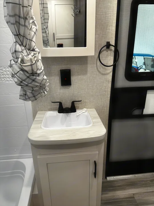 Modern **RV rental** bathroom with vanity, black faucet, plaid shower curtain, mirror, and wood-look floor.. Jayco Jay Flight 2024