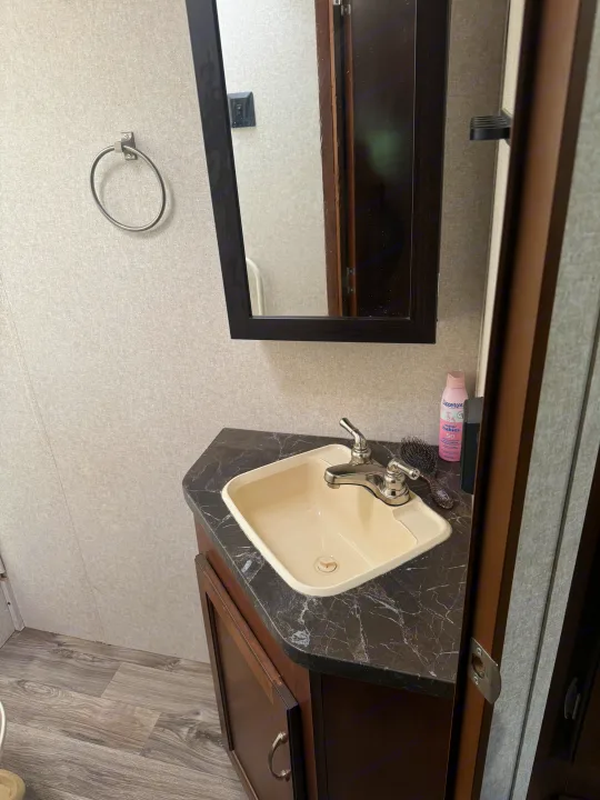 RV rental bathroom vanity features a compact sink, chrome faucet, mirror, and marble-look counter with essential items.. Jayco Jay Flight SLX Baja Edition 2017