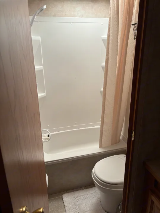 This RV rental bathroom features a white tub/shower combo, toilet, and a light-colored shower curtain.. Jayco Jay Flight 2004