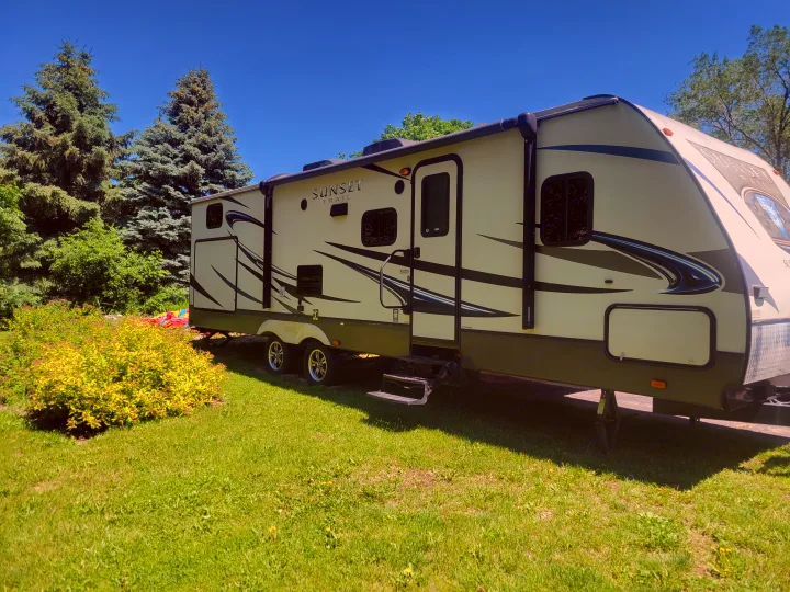 This Sunset Trail RV rental is parked on a sunny green lawn, with tall evergreen trees in the background.. Crossroads RV Sunset Trail Super Lite 2015