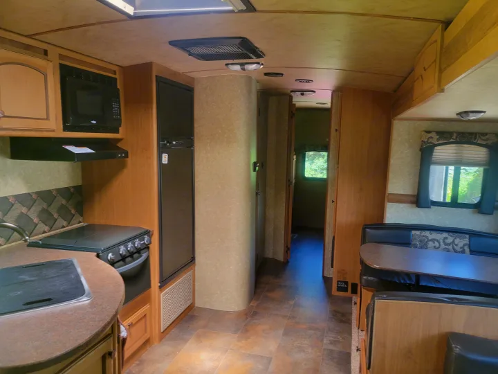 RV rental interior: kitchen with microwave, stove, fridge, and sink; plus a dinette and hallway. Warm wood accents.. Crossroads RV Sunset Trail Super Lite 2015