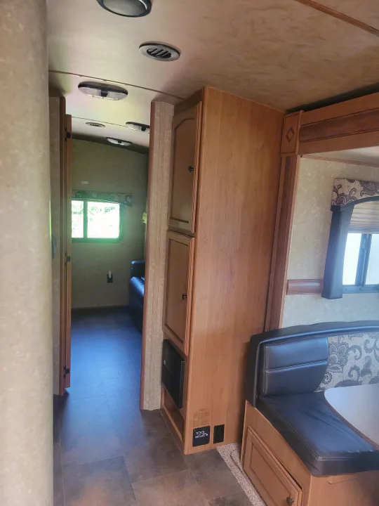 Inside an RV rental, showing a hallway, wooden cabinets, and a dinette seating area with dark cushions.. Crossroads RV Sunset Trail Super Lite 2015