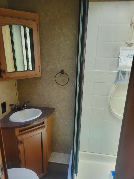 Compact RV rental bathroom features a corner sink, wooden vanity, mirror cabinet, shower with DampRid, and toilet.. Crossroads RV Sunset Trail Super Lite 2015