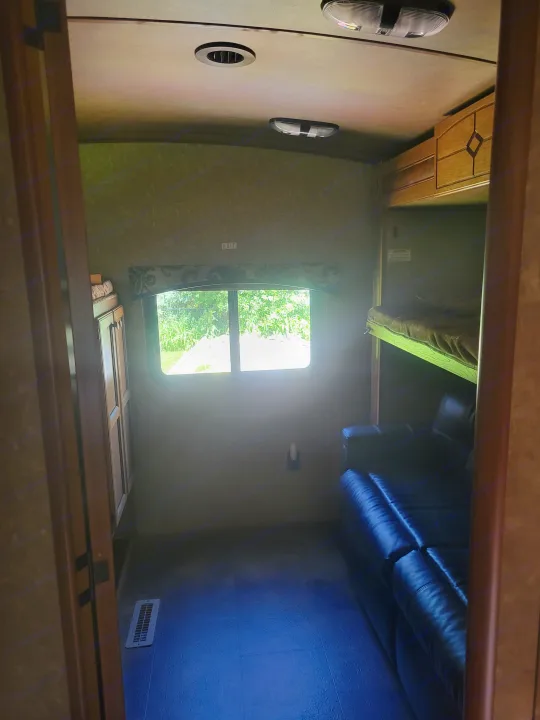 This RV rental interior features bunk beds, a bright window with green outdoor views, and a dark leather couch.. Crossroads RV Sunset Trail Super Lite 2015