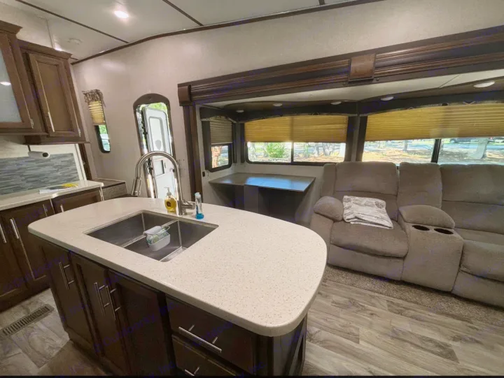 Spacious RV rental with a modern kitchen island, sink, and a cozy living area featuring a reclining sofa.. Keystone RV Cougar 2019