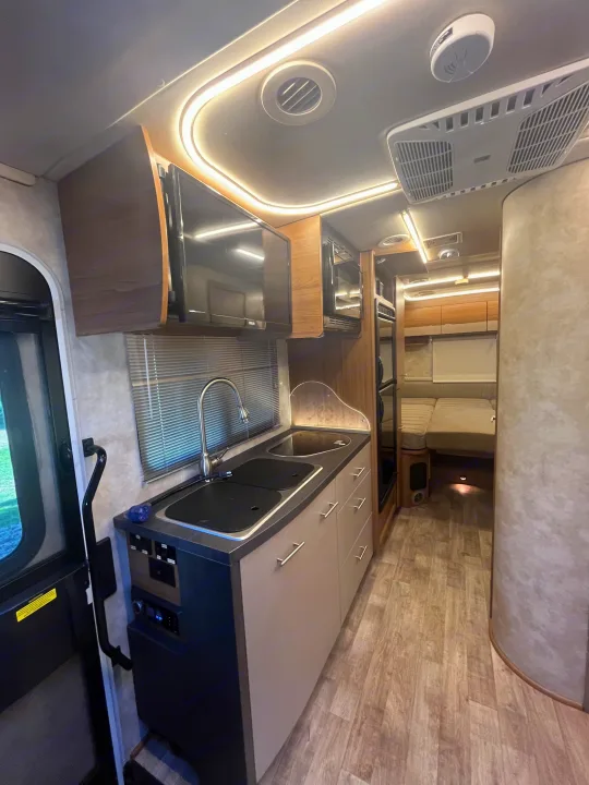 Inside a modern RV rental: well-equipped kitchen, cozy bed, and ambient lighting for comfortable travel.. Winnebago View 2019