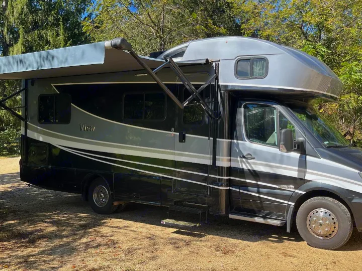 This sleek black & grey Class C RV rental, with its awning extended, is parked on a dirt lot.. Winnebago View 2019