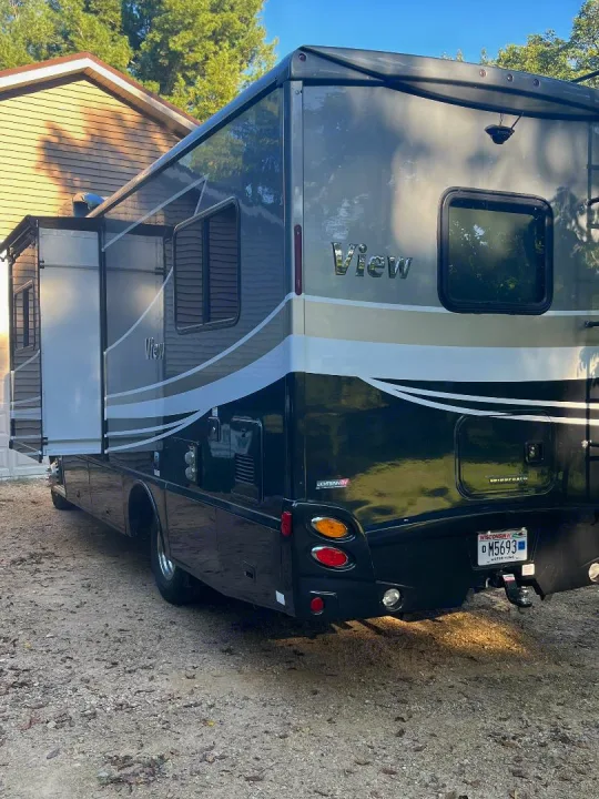 A dark Winnebago View motorhome, perfect for an RV rental, is parked on gravel with its slide-out extended.. Winnebago View 2019