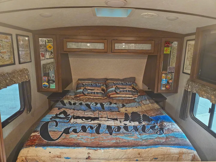 An RV rental bedroom with "Happy Camper" bedding, custom decals, ready for your next road trip.. Keystone RV Cougar 2019