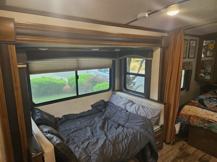 RV rental interior: cozy bedroom with dark bedding & windows, plus a second sleeping area, ideal for mobile living.. Keystone RV Cougar 2019
