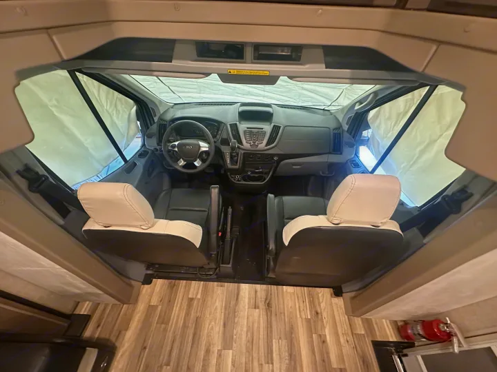 RV rental's inviting cockpit: modern dashboard, steering wheel, and comfortable two-tone seats. Windows are covered for privacy.. Winnebago Fuse 2017