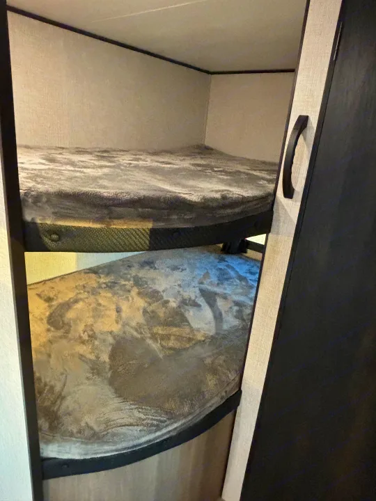 Inside an RV rental, two bunk beds with plush gray blankets offer cozy sleeping space.. Jayco Jay Flight SLX 2024