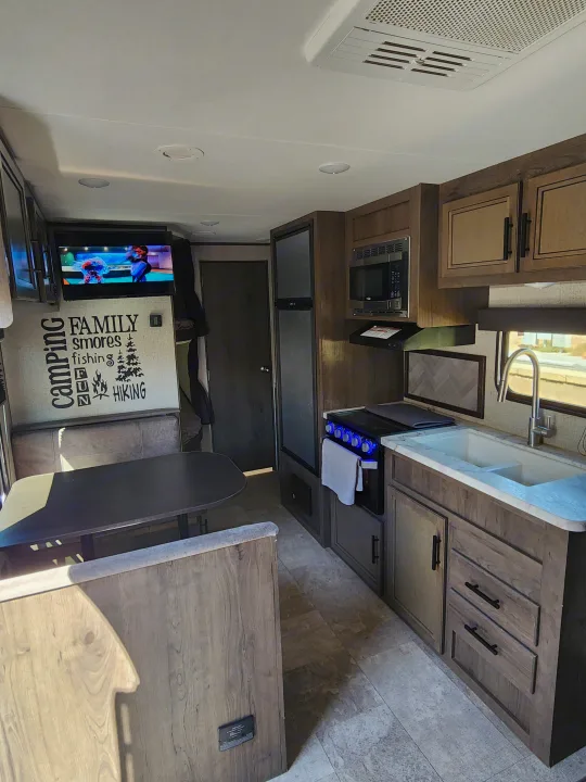 RV rental interior showing a cozy living/kitchen area with a dining booth, TV, and camping-themed wall decal.. Jayco Jay Flight SLX Rocky Mountain Edition 2020