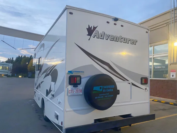 Rear view of a white Adventurer RV, likely an RV rental, showing its Alberta license plate and a nearby bubble tea shop.. Adventurer Adventurer Motorhome 2017
